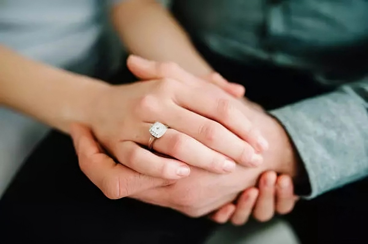 Gros plan sur une main de femme portant une bague de fiançailles en diamant, tenue par les mains de son partenaire, symbolisant l'engagement et l'amour.